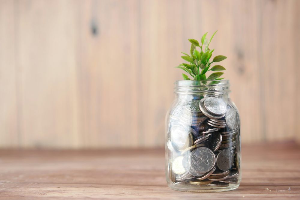 a glass jar with change in it and a plant growing out of it illustrating investing which is a smart money habit